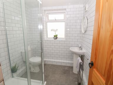 A bathroom with a shower cubicle toilet sink and window at Buarthau Cottage in Llanrug