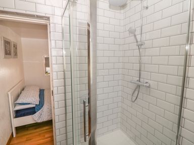 A bathroom with a glass shower enclosure and a tiled wall next to a bedroom with a bed and wall art at Buarthau Cottage in Llanrug
