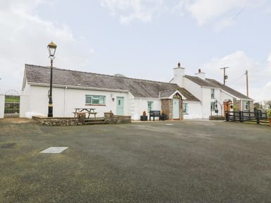 A white cottage with light blue doors and windows and a picnic table outside at Buarthau Cottage in Llanrug