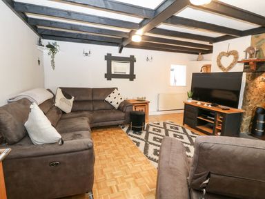 A living room with brown sofas a patterned rug a television on a wooden stand and exposed ceiling beams at Buarthau Cottage in Llanrug