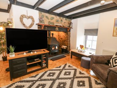 A living room with a television on a stand near a fireplace and a sofa at Buarthau Cottage in Llanrug