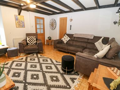 A living room with brown sofas a patterned rug and wooden doors at Buarthau Cottage in Llanrug