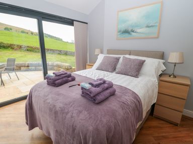 A bedroom with a double bed with purple bedding and towels beside large glass doors opening to a patio at Coal Drops in Alnwick