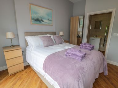 A bedroom with a double bed with purple blankets and towels bedside tables lamps wardrobe and an ensuite bathroom at Coal Drops in Alnwick