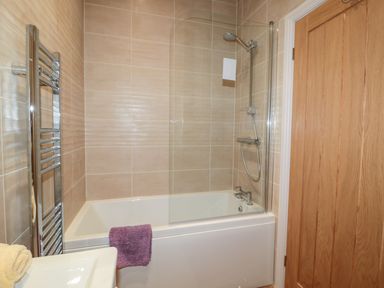 A bathroom with a bathtub shower combination a glass shower screen a chrome towel radiator and wooden door at Coal Drops in Alnwick