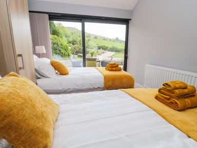 A bedroom with two single beds with yellow pillows and towels near a sliding glass door showing a garden outside at Coal Drops in Alnwick
