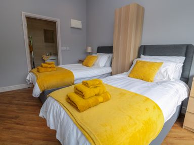 A bedroom with two single beds with yellow pillows towels and blankets at Coal Drops in Alnwick