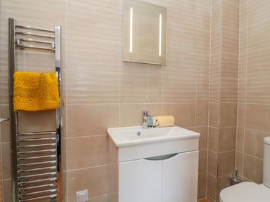 A bathroom with a white sink cabinet a mirror above a sink a chrome towel rack with a yellow towel and a toilet at Coal Drops in Alnwick