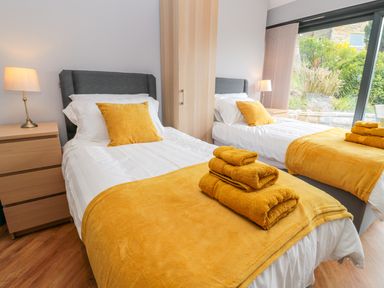 A bedroom with two single beds yellow blankets and pillows wooden nightstands lamps and a large window at Coal Drops in Alnwick