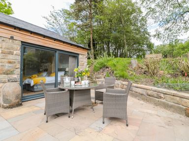 An outdoor patio with a round table and four wicker chairs next to a stone building with a sliding glass door at Coal Drops in Alnwick