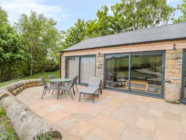 An outdoor patio with a table four chairs and a lounge chair outside a stone building with large sliding glass doors at Coal Drops in Alnwick
