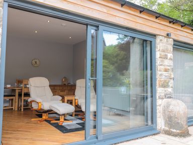 A room with two armchairs on a rug a wooden table and a dining table with chairs seen through a sliding glass door at Coal Drops in Alnwick