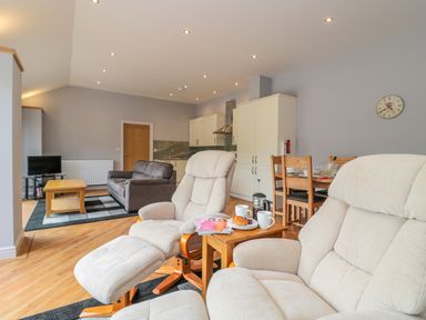 An open living room and kitchen with cream recliner chairs wooden coffee tables a brown sofa and a dining table at Coal Drops in Alnwick