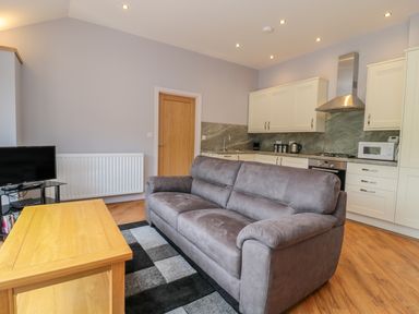 A living room with a grey sofa wooden coffee table and kitchen cabinets at Coal Drops in Alnwick