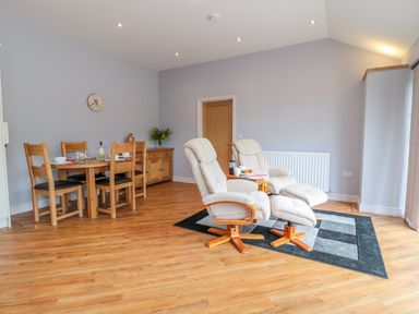 A living area with two reclining chairs on a rug and a wooden dining table with chairs at Coal Drops in Alnwick
