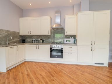 A kitchen with white cabinets a built in oven a microwave and a wooden floor at Coal Drops in Alnwick