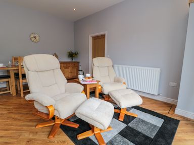 A living room with two beige armchairs and footrests on a patterned rug next to a wooden side table with cups and a teapot at Coal Drops in Alnwick