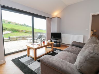 A living room with a gray sofa a wooden coffee table a television and large sliding glass doors at Coal Drops in Alnwick