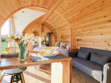 An interior wooden pod with a table set with bowls and plates a gray sofa a bed with pillows and folded towels and a vase of flowers at Chapel Pod in Callington