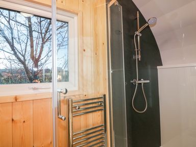 A bathroom with a window wooden walls a shower with a glass door and a metal towel rack at Chapel Pod in Callington