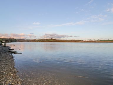 A calm river with a pebbled bank and grassy hills in the background at Chapel Pod in Callington
