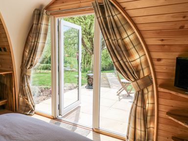 A bedroom with a bed and plaid curtains by glass doors opening to a garden at Chapel Pod in Callington
