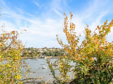 A view of boats on water with trees in the foreground and houses on a hill across the water at The Old Cows House in Helston