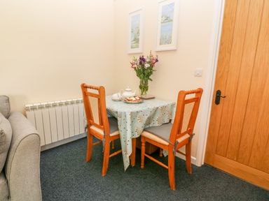 A small dining area with two wooden chairs and a table with a tablecloth flowers and tea set at The Old Cows House in Helston