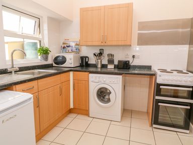 A kitchen with wooden cabinets a washing machine a microwave a kettle and a stove at The Old Cows House in Helston