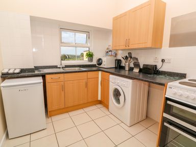 A kitchen with wooden cabinets a washing machine a stove a refrigerator and a window at The Old Cows House in Helston