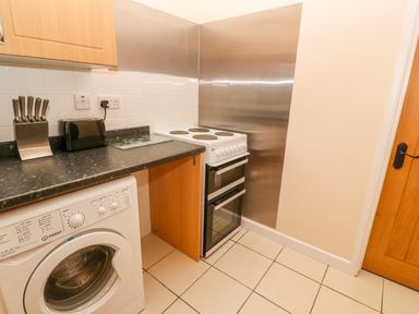 A kitchen with a washing machine a knife block a toaster and an electric stove at The Old Cows House in Helston