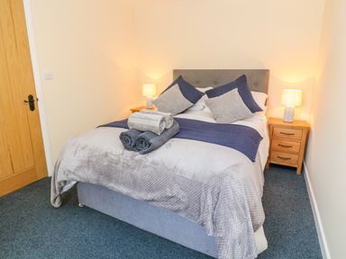A bedroom with a bed with blue and grey bedding and pillows two bedside tables with lamps at The Old Cows House in Helston