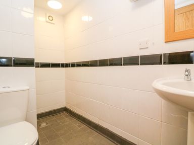 A bathroom with a toilet sink mirror and tiled walls and floor at The Old Cows House in Helston