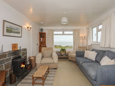 A living room with a fireplace armchairs a blue sofa and a window with a sea view at Allt y Mor in Harlech