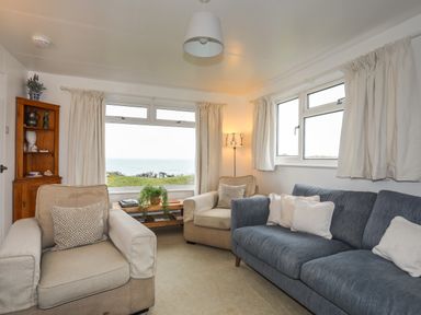 A living room with armchairs a sofa a wooden corner cabinet and windows overlooking grass and water at Allt y Mor in Harlech