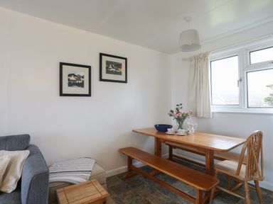 A dining area with a wooden table bench and chair next to a window with curtains and a sofa with cushions at Allt y Mor in Harlech