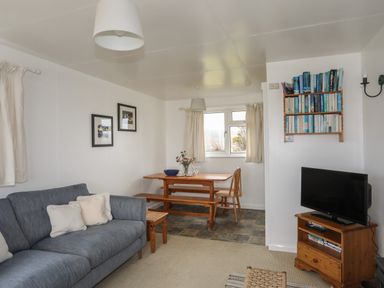 A living room with a blue sofa, wooden dining table, books on a wall shelf and a television at Allt y Mor Harlech