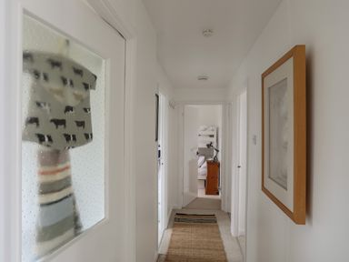 A hallway with a rug on the floor a framed picture on the wall and a bedroom with bunk beds visible through an open door at Allt y Mor in Harlech