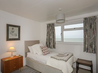 A bedroom with a single bed, bedside table with lamp, framed artwork, window with curtains, and a small wooden stool at Allt y Mor in Harlech