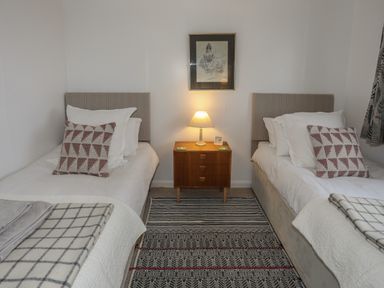 A bedroom with two single beds a wooden nightstand with a lamp and a framed picture on the wall at Allt y Mor in Harlech