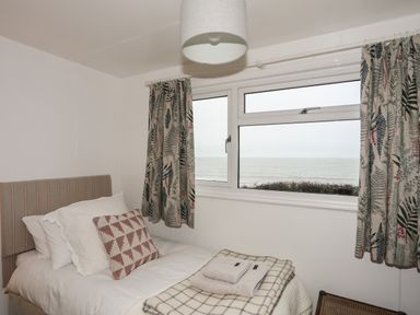 A bedroom with a single bed near a window showing an ocean view at Allt y Mor in Harlech
