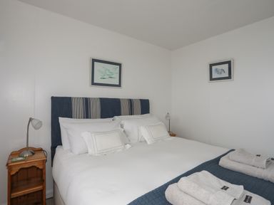 A bedroom with a double bed and striped headboard bedside tables with lamps and framed pictures on the walls at Allt y Mor in Harlech
