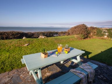 A picnic table with a pitcher of orange drink apples plants and magazines in a garden overlooking the sea at Allt y Mor in Harlech