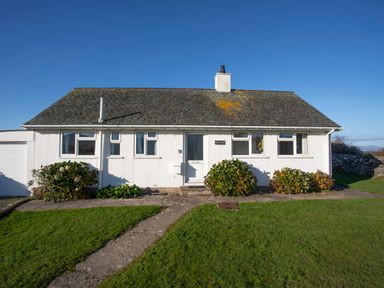 A white single-story house with a tiled roof and three bushes in front at Allt y Mor in Harlech