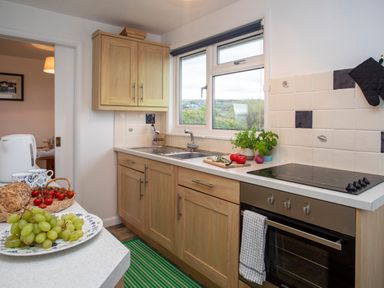 A kitchen with wooden cabinets a sink an oven and a counter with grapes bread and tomatoes at Allt y Mor in Harlech
