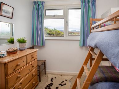 A bedroom with bunk beds wooden dresser a chair and a window with curtains at Allt y Mor in Harlech