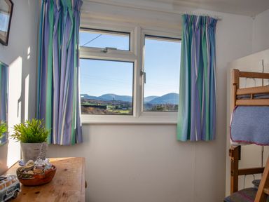 A small room with a window showing mountains curtains a wooden table with a plant and a bowl and a wooden bunk bed at Allt y Mor in Harlech