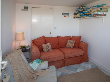 A small sitting room with an orange sofa a light blue armchair a lamp and a shelf of board games at Allt y Mor in Harlech