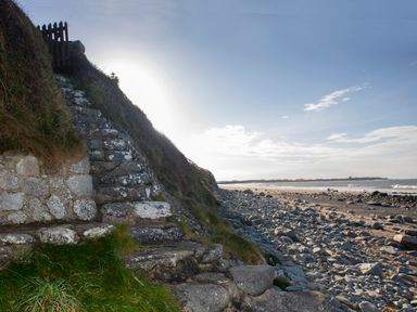 Stone steps leading up a grassy hill beside a rocky beach with ocean and sky in the background at Allt y Mor in Harlech
