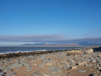 A rocky beach with sand and small waves with mountains in the background at Allt y Mor in Harlech